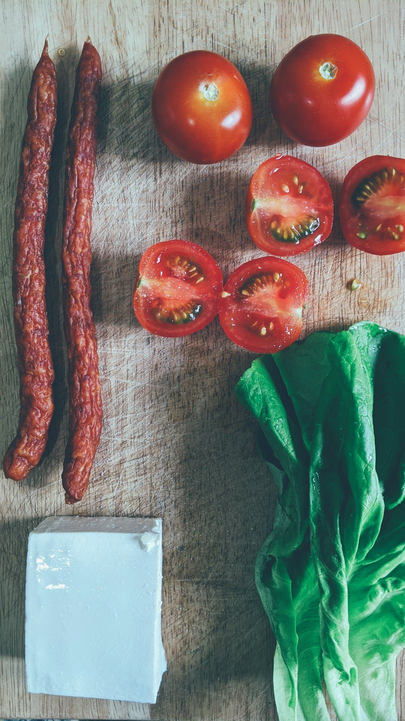 Wurst, Tomaten, Salat und Käse auf einem Holzschneidebrett.
